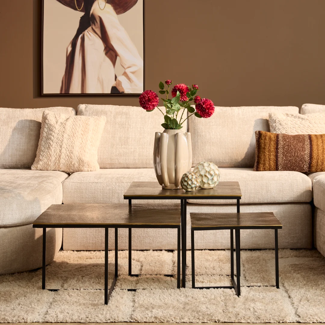 Drie roest salontafels van metaal met zwarte poten op een zacht kleed. Een beige bank met kussens en bloemenvaas op de tafels.