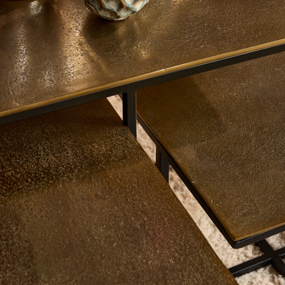 Detailopname van een roestkleurige salontafel set met zwarte metalen frame. Warm licht accentueert de textuur van het tafelblad.