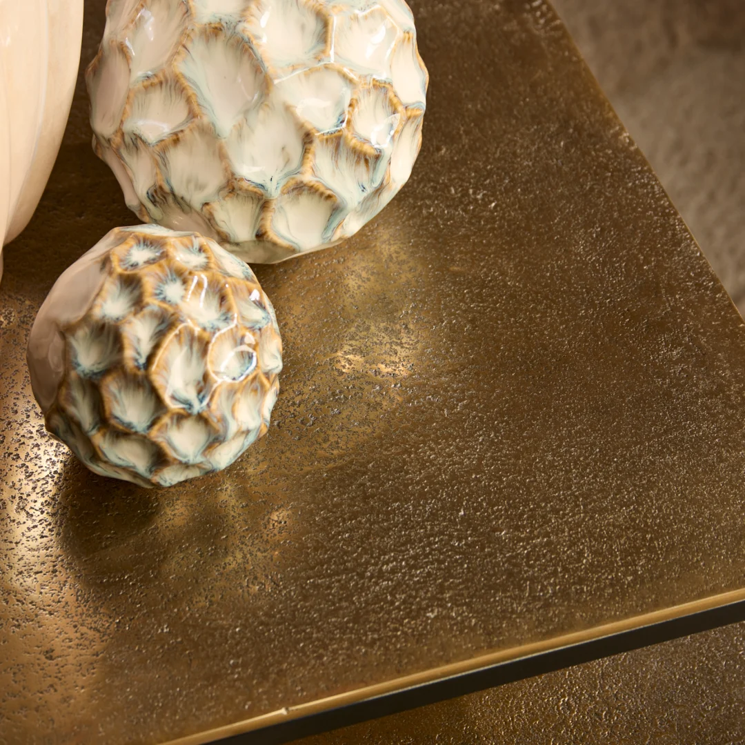 Detailopname van een roestkleurige salontafel met decoratieve bollen. Gouden tinten en textuur van het tafelblad zijn goed zichtbaar.