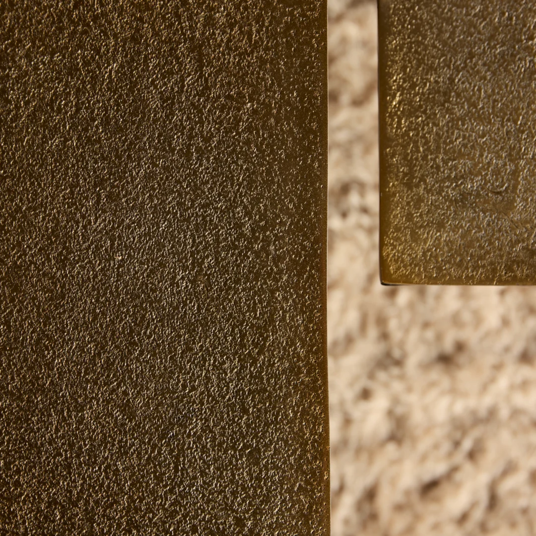 Detailopname van een roestkleurige salontafel met een ruwe textuur. De tafel heeft een vierkant design en is gemaakt van metaal. Warm licht.