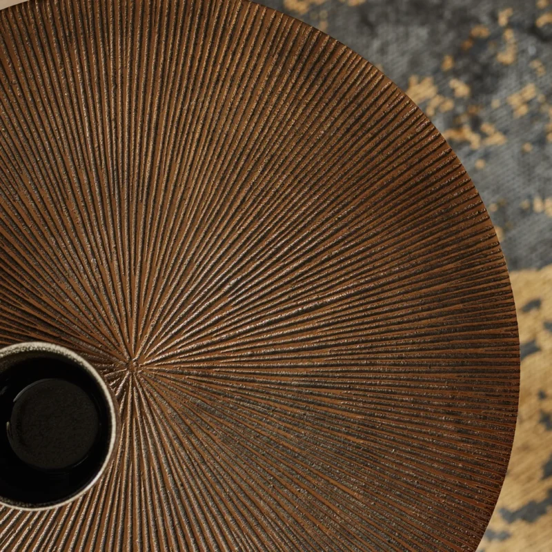 Een close-up bovenaanzicht van de Salontafel 40 x 50 CM Vierkant met een gestructureerd, radiaal lijnenpatroon en een klein zwart-wit keramisch kopje op de rand. Een blauw en beige abstract vloerkleed is zichtbaar op de achtergrond.