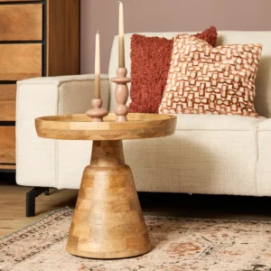 De bijzettafel Troy, een rond houten stuk, heeft twee hoge kaarsen en staat voor een crèmekleurige bank met kussens met patroon op een vloerkleed met patroon in een gezellige woonkamer.