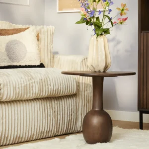 Een moderne woonkamer met een gestructureerde crèmekleurige bank, de ronde bruine houten bijzettafel Donna, een beige vaas met kleurrijke bloemen en een zacht wit vloerkleed op de vloer.