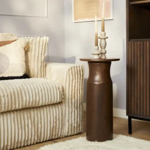 Een gezellige woonkamer heeft een beige ribfluwelen bank, de bijzettafel Mason met twee beige kaarsen op houten houders en een crèmekleurig tapijt op een houten vloer. Kunstwerken versieren de lichtgekleurde muur.