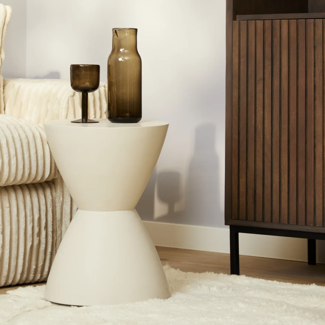 Een moderne woonkamer met de crèmekleurige bijzettafel Abbey met twee bruine glazen vazen, geplaatst naast een crèmekleurige gestructureerde bank en een donkerhouten kast op een wit pluche vloerkleed.