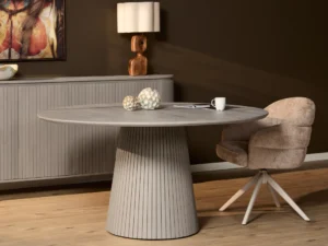 Grijze Solana eettafel met ronde vorm en verticale lijnen op de voet. Een beige stoel en houten vloer in een interieur met zachte belichting.