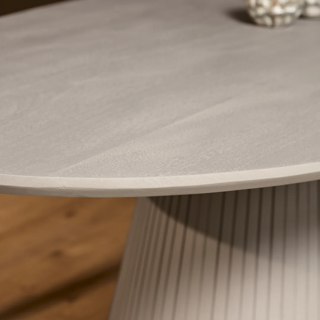 Detailopname van de ovale eettafel Solana met een grijze afwerking. De basis heeft een verticale ribbelstructuur. Zachte belichting.