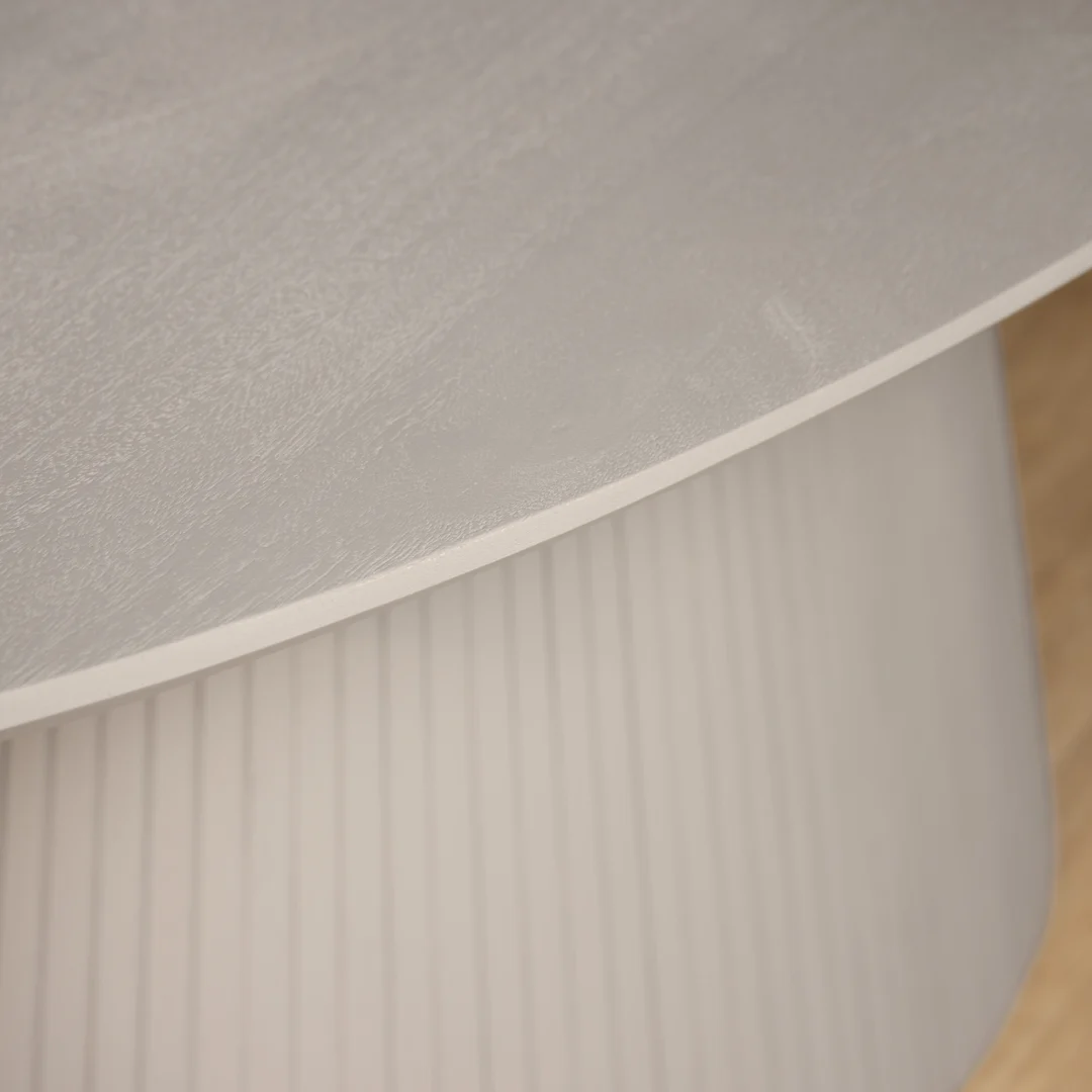 Detailopname van een witte Solana eettafel met een ovaal blad en een gestreept onderstel. Zachte belichting en een lichte houten vloer.