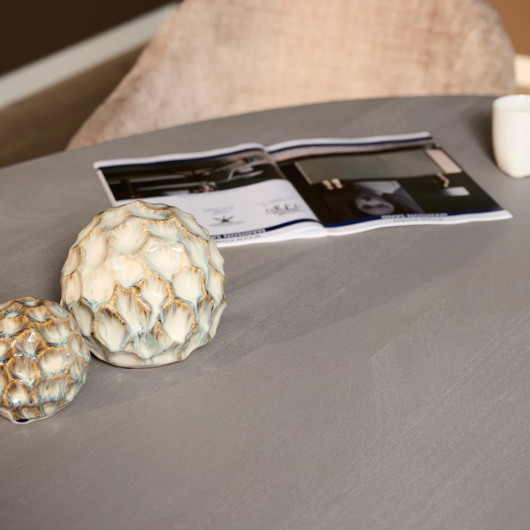 Detailopname van een Solana eettafel met keramische decoratie en een open tijdschrift. Zachte belichting en neutrale grijze tinten.