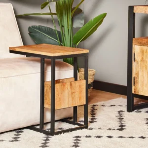 De Schuifregelaar Natuurlijk mangohout, een moderne C-vormige bijzettafel met een blad van natuurlijk mangohout en een zwart metalen onderstel, staat naast een lichte bank op een vloerkleed met patroon, met een grote groene plant op de achtergrond.