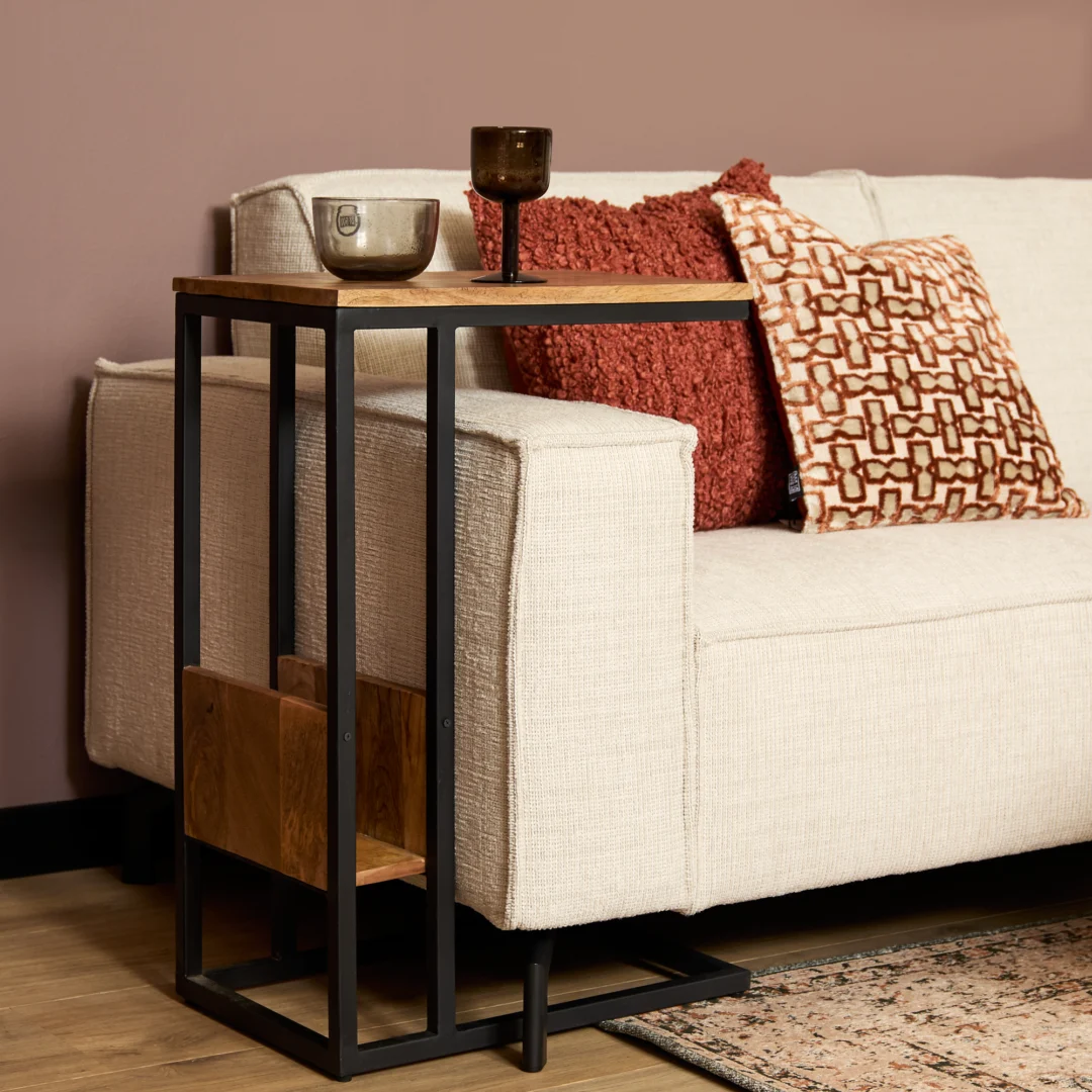 De Schuifregelaar Naturel zit naast een beige bank versierd met rode kussens en kussens met patronen. Twee glazen rusten op de tafel, terwijl de bank tegen een mauve muur staat.