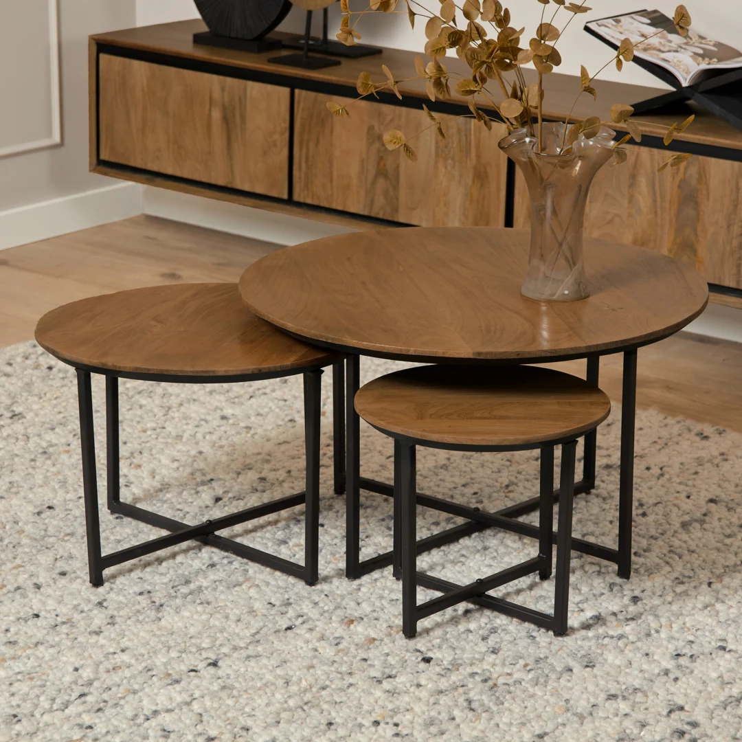 Houten salontafel set van drie ronde tafels met zwart metalen onderstel op een wit vloerkleed, zachte belichting.