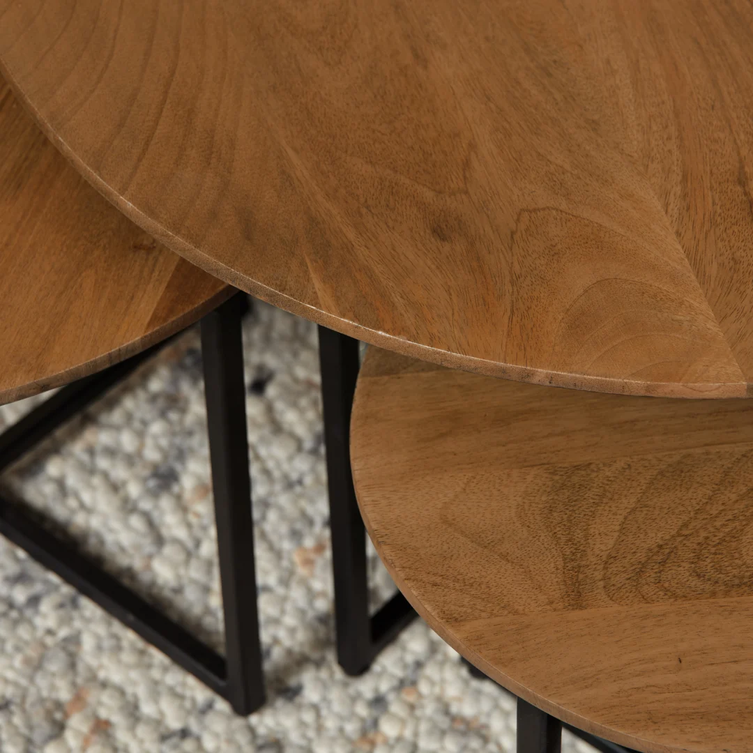 Close-up van een set houten salontafels met opbergruimte en een zwart metalen frame, op een zacht kleed. Warme, natuurlijke belichting.