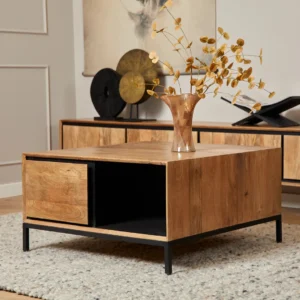 De Salontafel 80 CM Design, een moderne houten salontafel met zwarte metalen poten, staat op een vloerkleed met structuur. Een glazen vaas met gedroogde takken siert de tafel, terwijl houten kasten en abstracte muurkunst de gezellige leefruimte compleet maken.