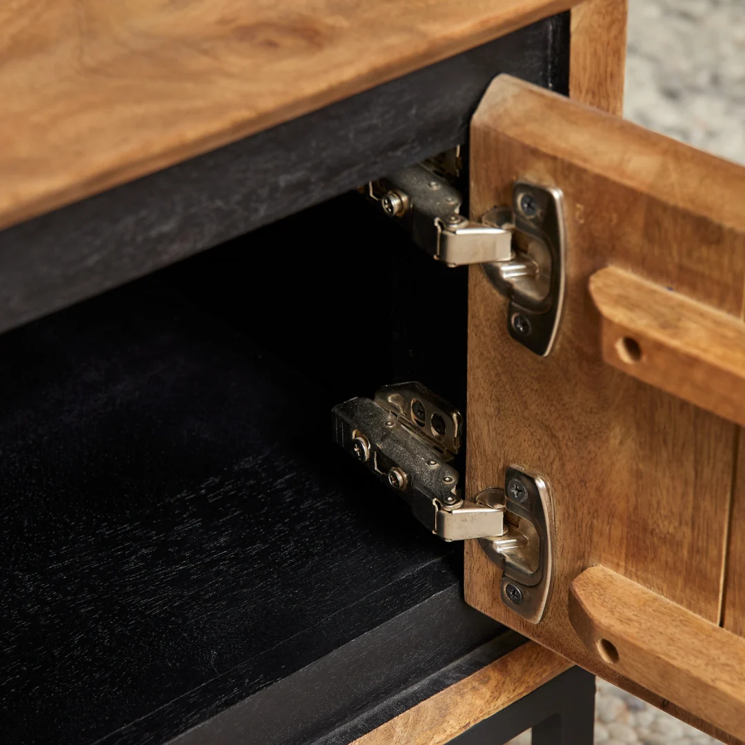 Detailopname van de binnenkant van een houten salontafel, met zwarte binnenkant en zilverkleurige scharnieren, open kastdeur, warme belichting.