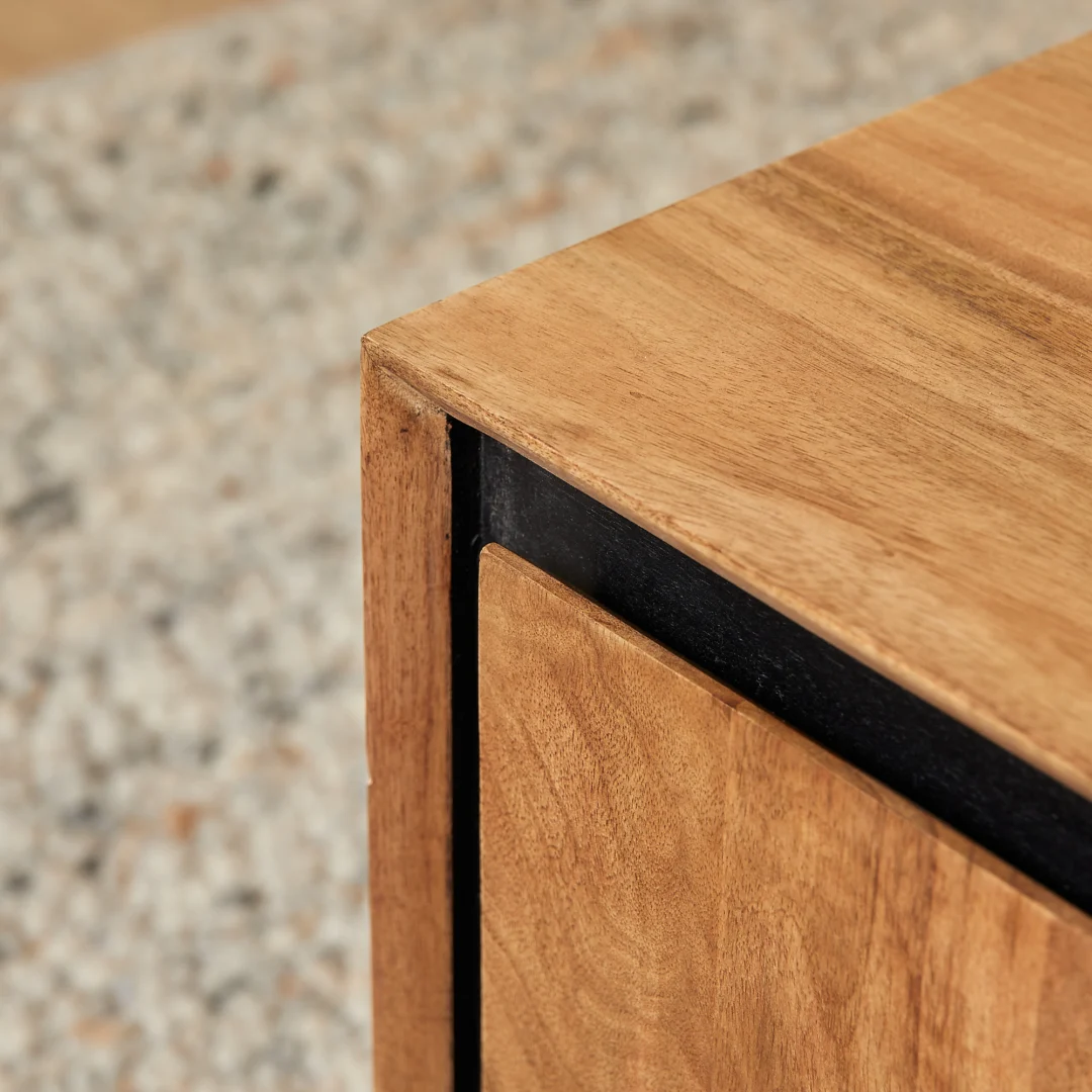 Close-up van de hoek van de Bijzettafel RichWood | 60 cm, met een gladde houten afwerking met een zwart metalen accent, tegen een zacht vervaagde, gespikkelde achtergrond.