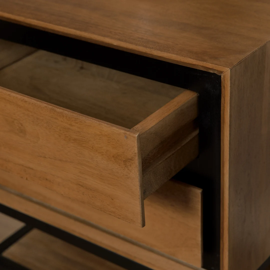 Houten nachtkastje met open lade, schuin van boven gefotografeerd. De lade is lichtbruin, de kast heeft zwarte accenten. Zachte belichting.