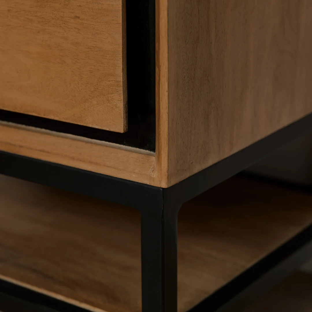 Detailopname van een houten nachtkastje met lade, zwarte metalen poten en een open plank. Neutrale belichting, warme houttinten.