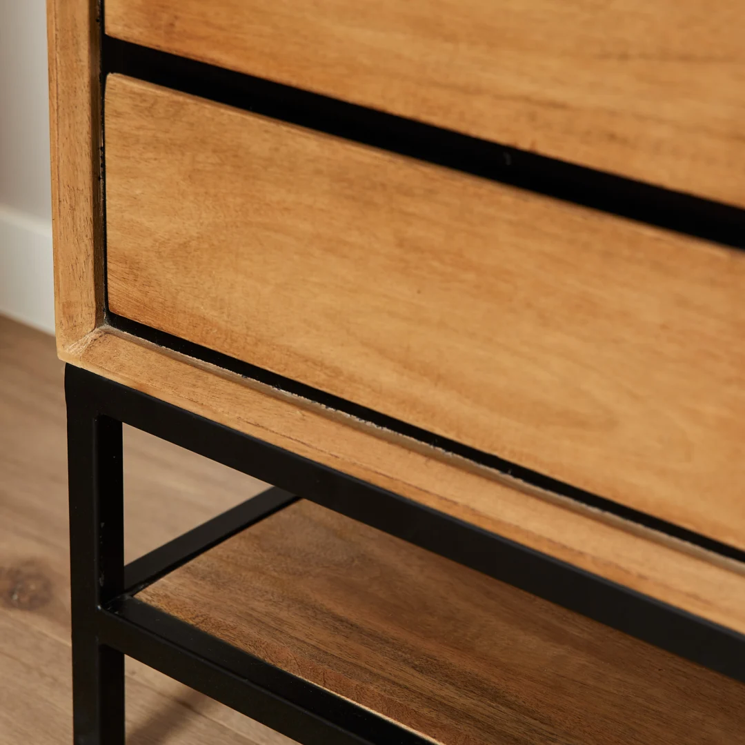 Detailopname van een houten nachtkastje met lade en zwart metalen frame. Warme belichting, houten vloer. Functioneel slaapkamer meubel.