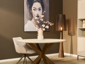 Eettafel Madison naturel met een rond blad en een metalen onderstel in een interieur met een schilderij en een lamp. Lichte kleuren.
