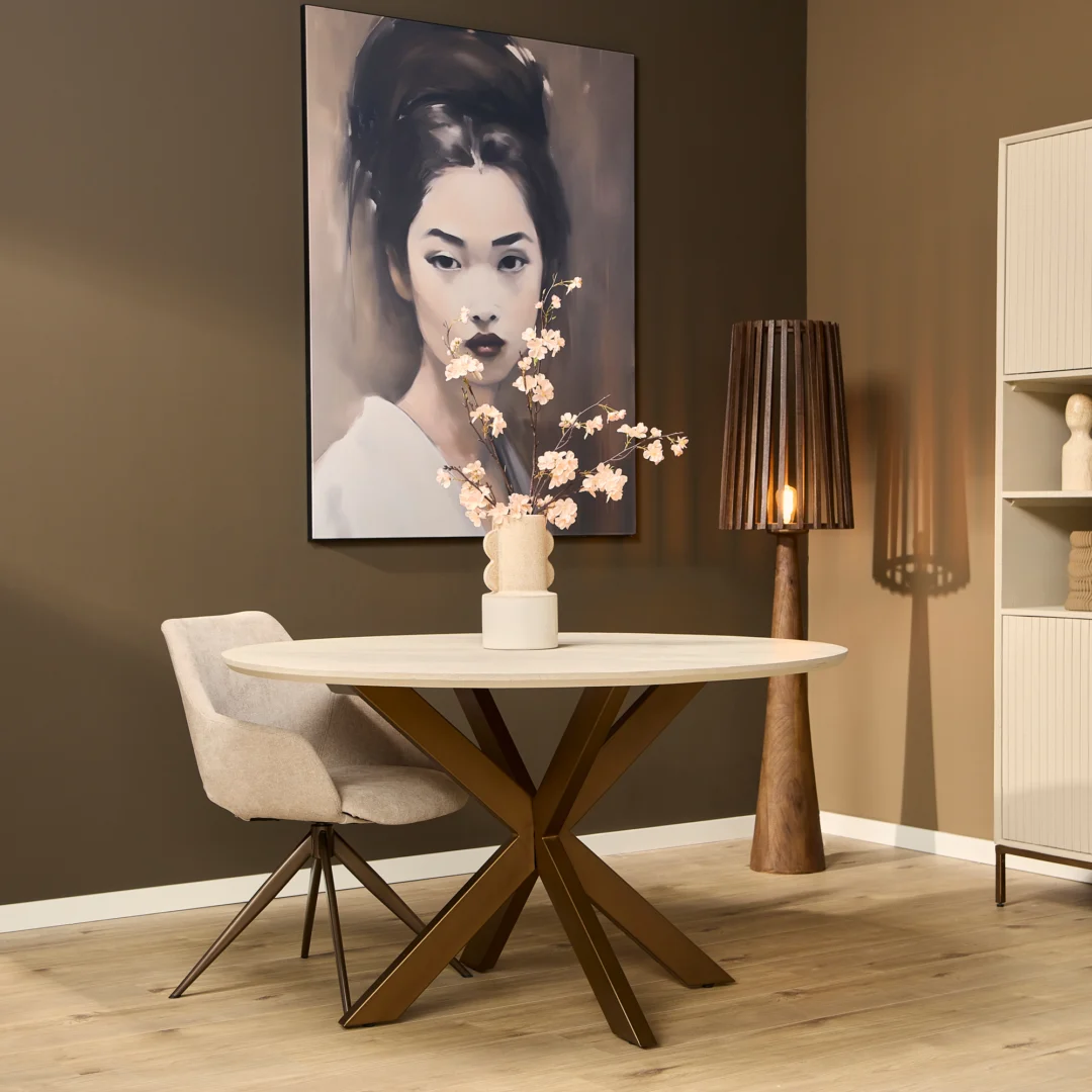 Eettafel Madison naturel met een rond blad en een metalen onderstel in een interieur met een schilderij en een lamp. Lichte kleuren.