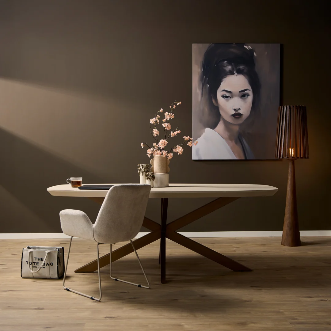 Een moderne eethoek met de Eettafel Madison Sand (160 cm, Deens Ovaal), een stoel met kussens, een vaas met roze bloemen, een hoge staande lamp, een tas op de vloer en een groot portret van een donkerharige vrouw aan de muur.