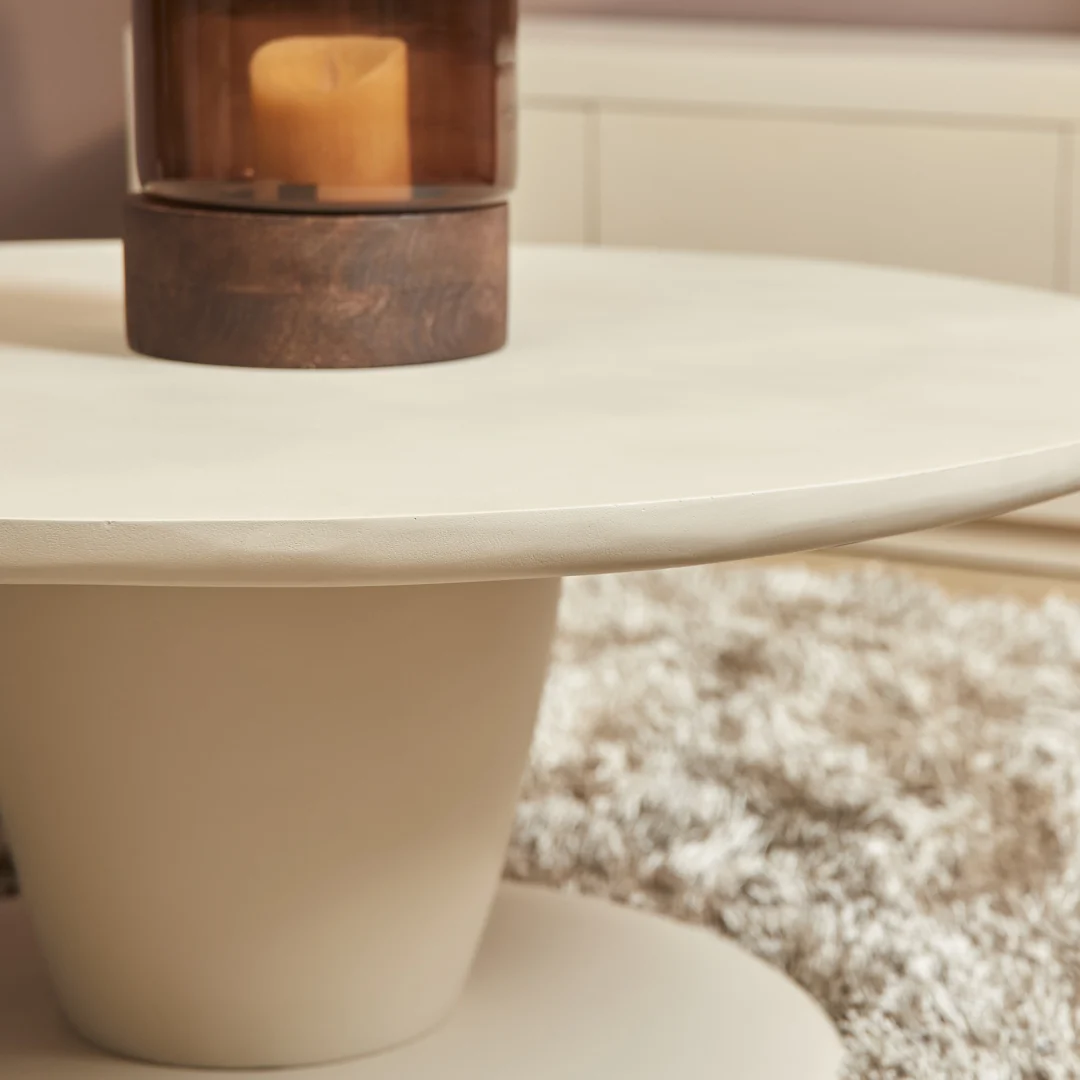 Beige salontafel met een ronde vorm en een kaars in een glazen houder. Zachte belichting en een zachte, pluizige achtergrond.