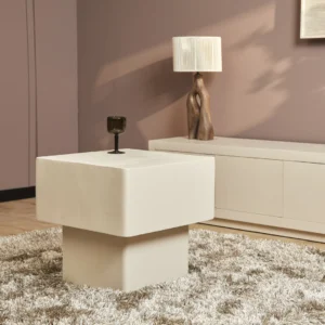 In een moderne woonkamer staat de Salontafel 57 x 52 CM Vierkant, een vierkante crèmekleurige tafel op een ruig tapijt, met een donker glas bovenop, een wit dressoir, een sculpturale lamp en mauve muren.