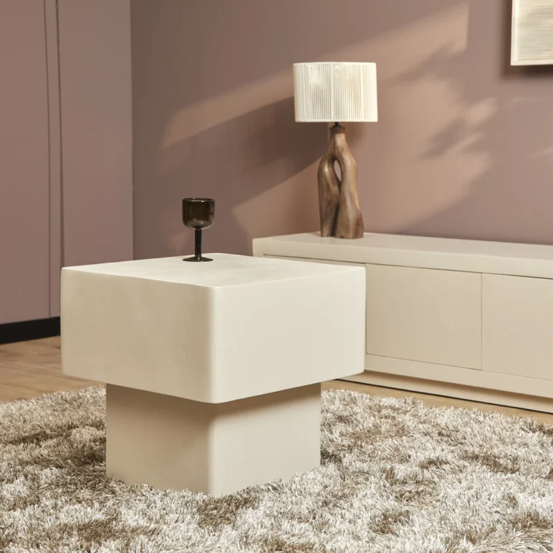 In een moderne woonkamer staat de Salontafel 57 x 52 CM Vierkant, een vierkante crèmekleurige tafel op een ruig tapijt, met een donker glas bovenop, een wit dressoir, een sculpturale lamp en mauve muren.