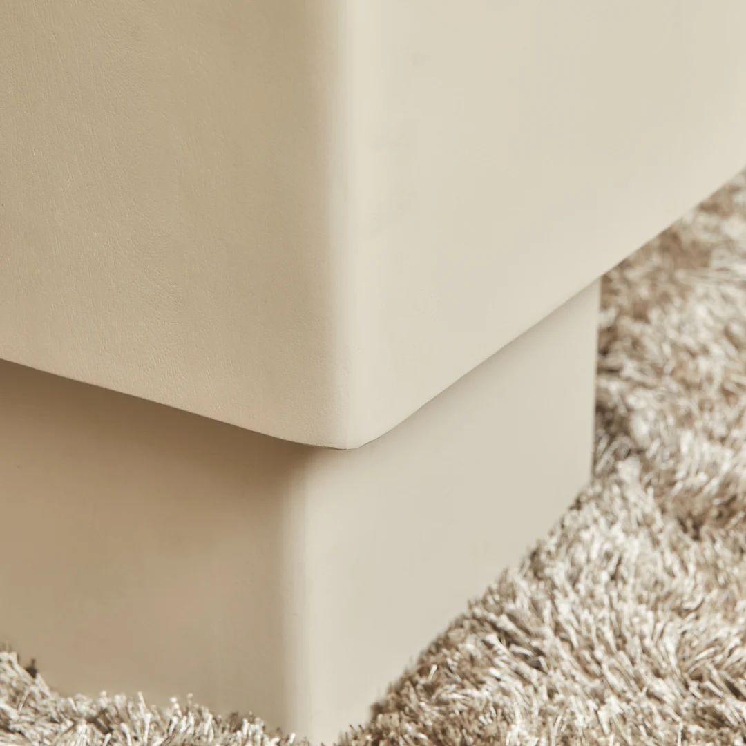 Close-up van de hoek van de Salontafel 57 x 52 CM Vierkant in lichtbeige, met een zacht, glad oppervlak en rustend op een gestructureerd, ruig lichtbruin tapijt.