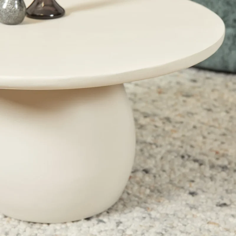 De Salontafel 70 CM Vierkant, een moderne crèmekleurige salontafel met een dik onderstel, staat op een licht getextureerd tapijt. Zilveren en donkere decorstukken zijn gedeeltelijk zichtbaar bovenop de tafel.