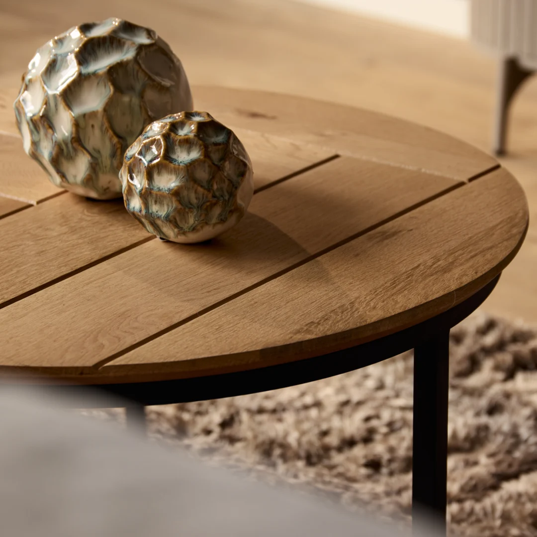 Detailopname van een ronde salontafel van eikenhout met decoratieve keramische bollen. Zachte belichting, warme kleuren.