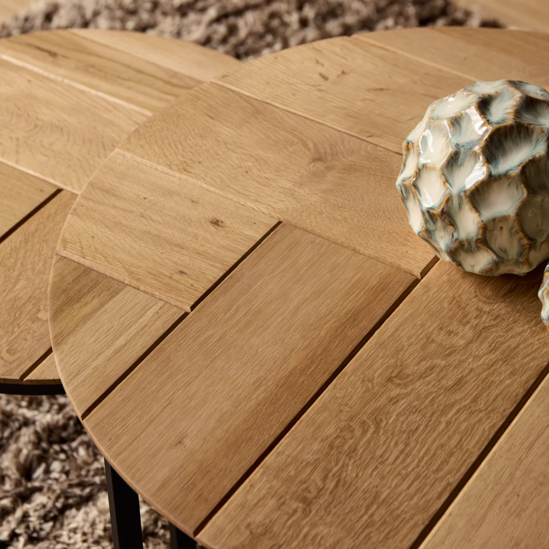 Detailopname van een ronde salontafel van eikenhout, met een keramische bol. Warme tinten en zachte belichting.