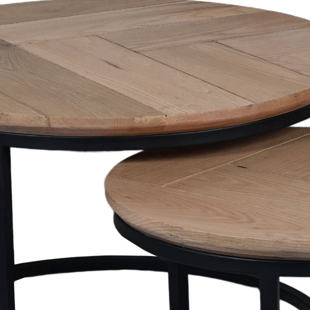 Detailopname van een set ronde salontafels. Bladen van eikenhout met visgraatmotief en een zwart metalen onderstel. Lichte tinten.