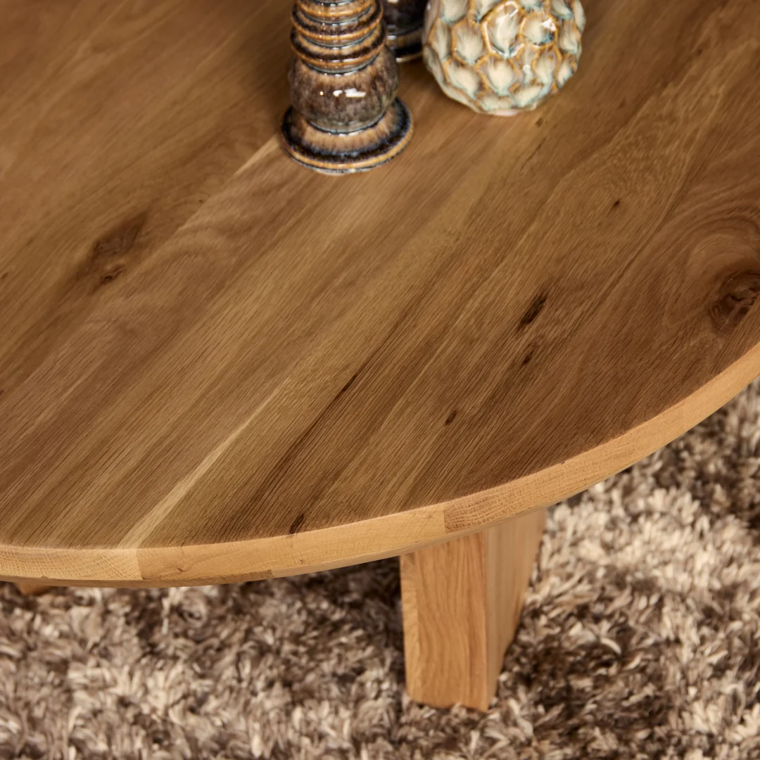 Close-up bovenaanzicht van een ronde salontafel van eikenhout met decoratieve objecten. Het hout heeft een warme, natuurlijke kleur.