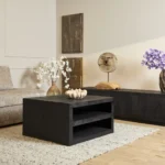 Een moderne woonkamer met Salontafel Zwart Design Tijdloos Design, een beige bank, neutrale inrichting, vazen met witte en paarse bloemen, abstracte muurkunst, een dressoir met structuur en een licht geweven vloerkleed.