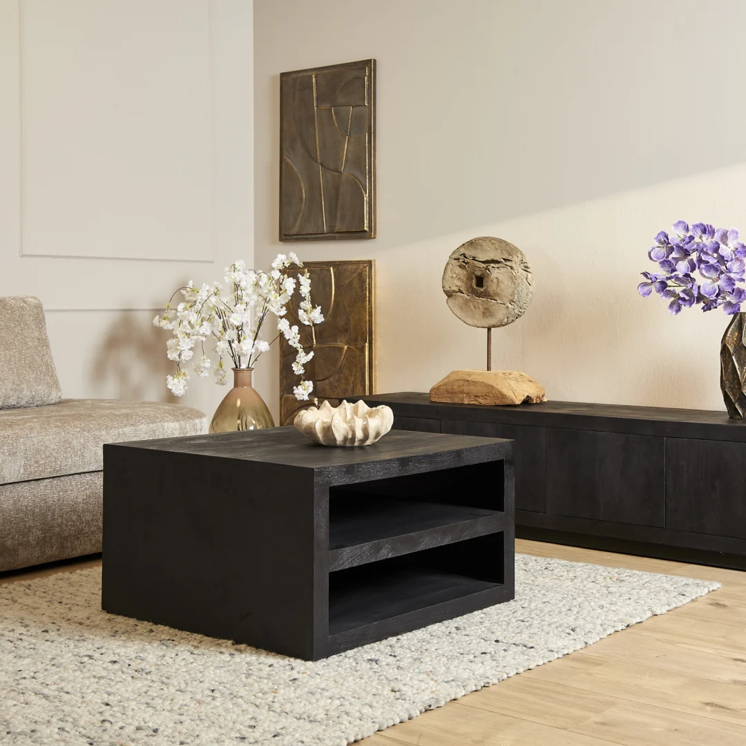 Een moderne woonkamer met Salontafel Zwart Design Tijdloos Design, een beige bank, neutrale inrichting, vazen met witte en paarse bloemen, abstracte muurkunst, een dressoir met structuur en een licht geweven vloerkleed.