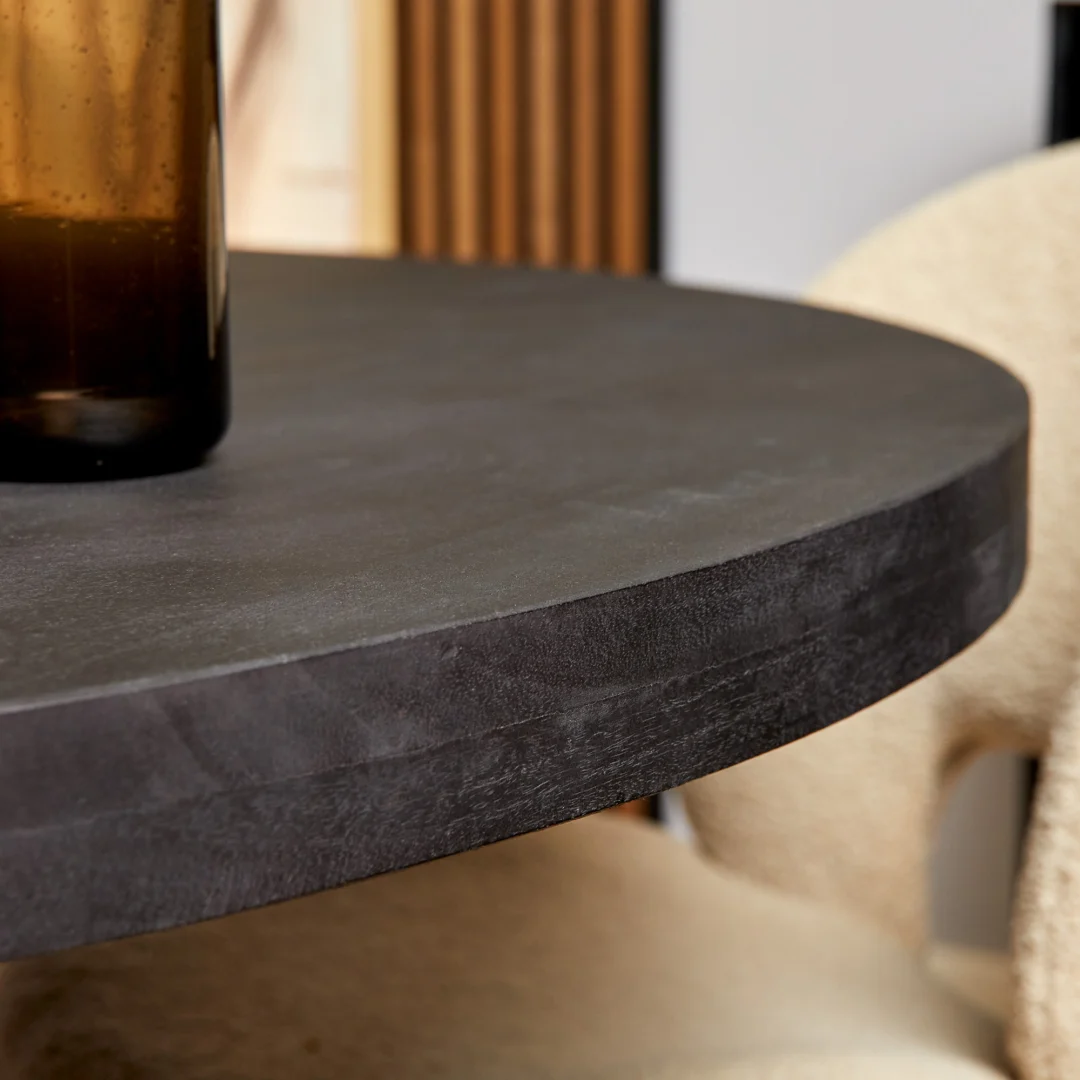 Een close-up van de Eettafel Denver Zwart, een ronde tafel van 120 cm, met een bruine glazen fles erop en crèmekleurige stoelen met structuur zichtbaar op de achtergrond.