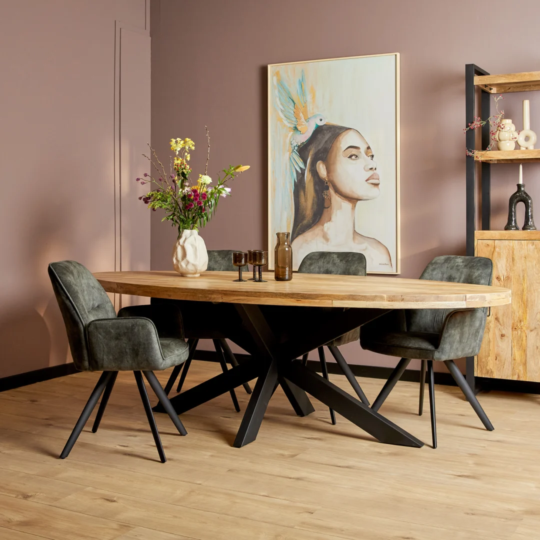 Een moderne eetkamer met de Eettafel Denver Ovaal mangohout 210 cm, vier grijs gestoffeerde stoelen, een vaas met bloemen, decoratieve flessen en een groot portret van een vrouw met een vogel op haar hoofd op een mauve muur.