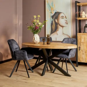 Een stijlvolle eethoek met de Eettafel Denver Ovaal Mangohout 180 cm tafel, drie grijs gestoffeerde stoelen, een bloemenvaas en een groot portret van een vrouw met een vogel op haar hoofd. De kamer heeft een houten vloer en gedempte muren.