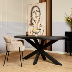 Een moderne eetkamer met de Eettafel Denver Zwart Ovaal 160 cm, een beige gestoffeerde stoel, fruitschaal en glazen op tafel, een groot vrouwenportret, een vaas met bloemen op de achtergrond, een lichthouten vloer en neutrale muren.