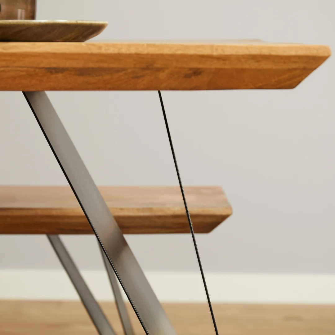 Close-up van de Eettafel Extense | 240 cm, een moderne houten tafel met metalen poten en een bijpassende bank eronder, beide met een licht houten oppervlak. De achtergrond bestaat uit een neutrale muur en een houten vloer.