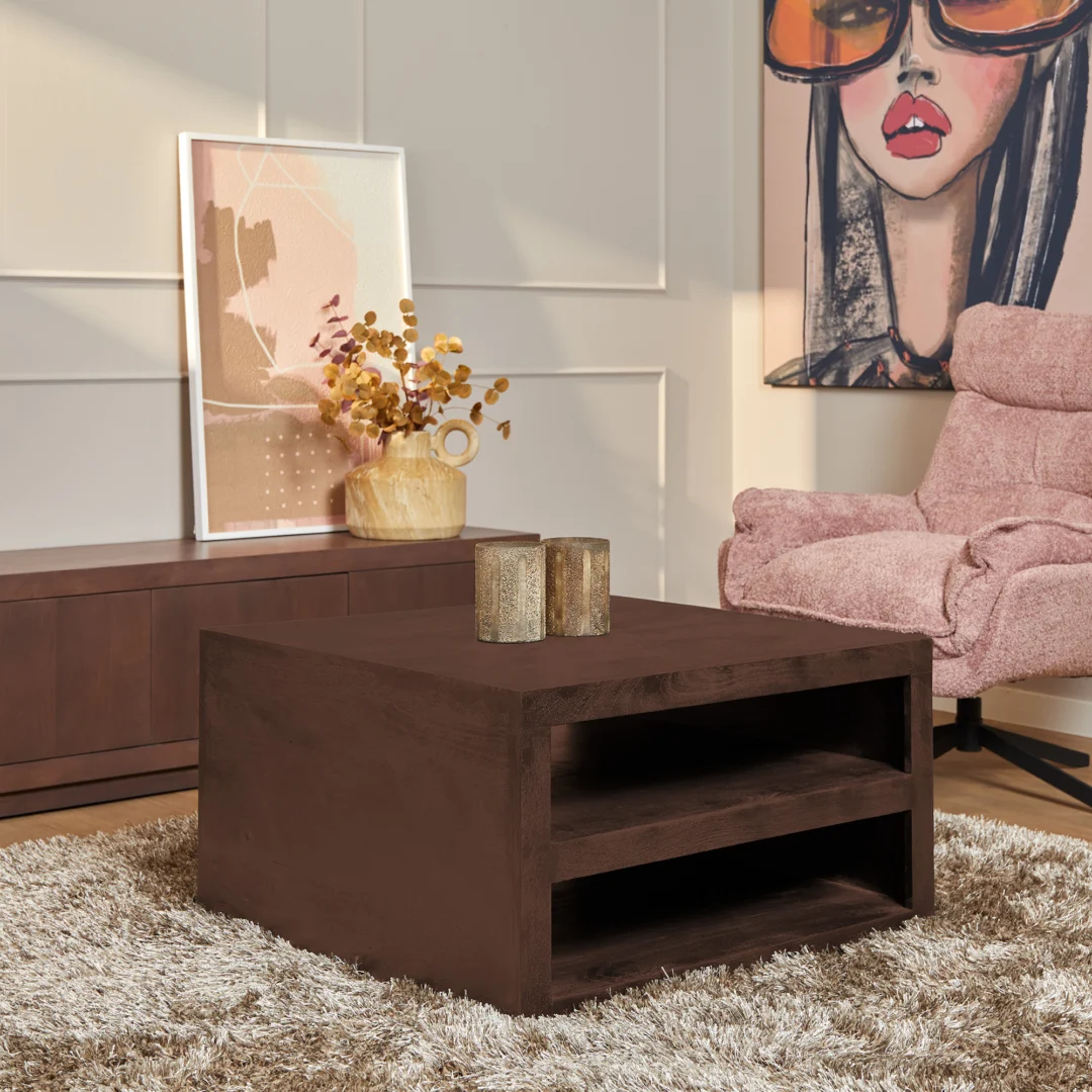 Een moderne woonkamer met de Salontafel Walnoot Compact op een shaggy licht vloerkleed, muurkunst, een roze fauteuil met structuur en een dressoir versierd met decoratieve items zoals een vaas met gedroogde bloemen.