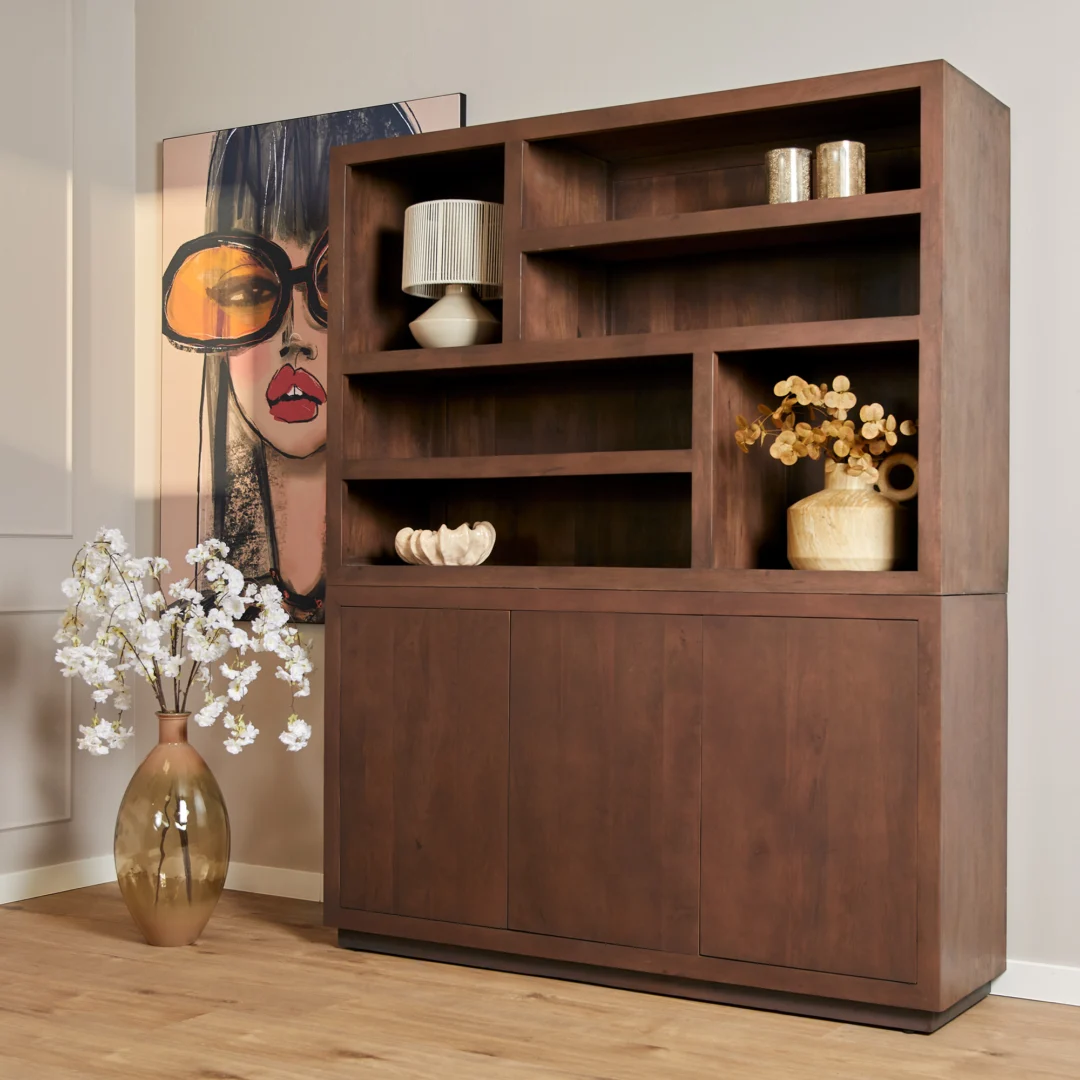 De Salontafel Walnoot Compact staat naast een hoge vaas met witte bloemen, terwijl een groot kunstwerk van een vrouwengezicht met bril tegen de muur leunt en een modern accent in de kamer creëert.