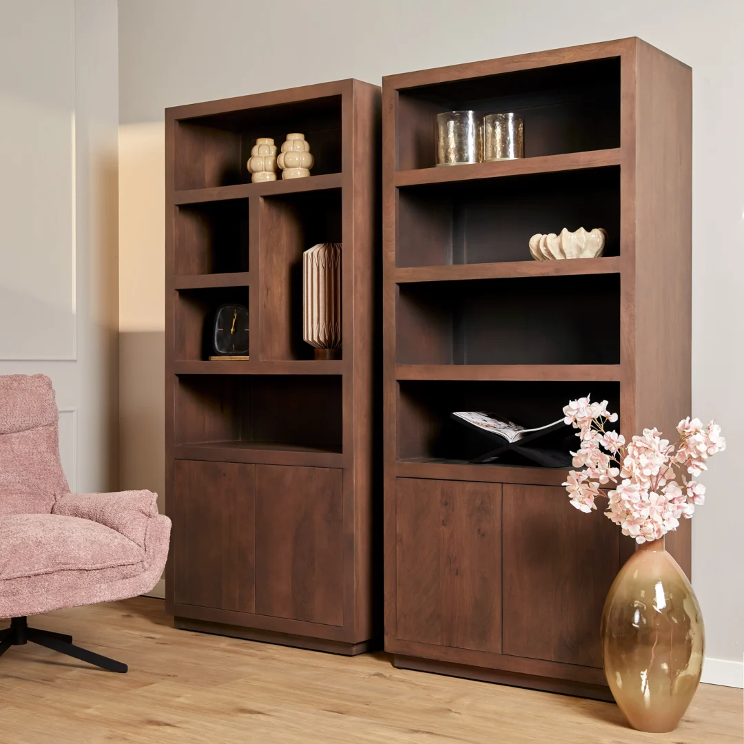 Salontafel Walnoot Compact ligt op een houten vloer tegen lichtgekleurde muren, met hoge houten boekenkasten met vazen en glaswerk. Een roze gestoffeerde stoel staat links en een grote vaas met roze bloemen staat rechts.