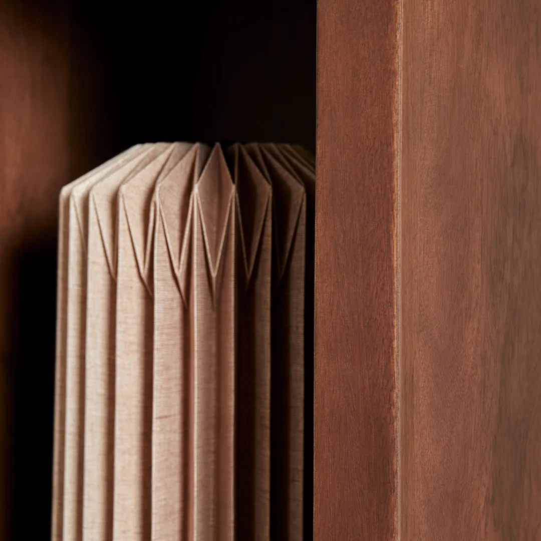 Een close-up van het houten oppervlak van Salontafel Walnoot Compact naast een geometrisch, geplooid object met textuur - waarschijnlijk papier of stof - tegen een donkere achtergrond.