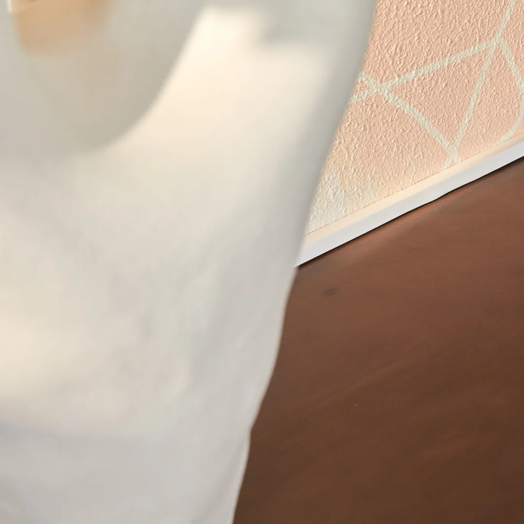 Close-up van een wit sculpturaal object op de voorgrond, met de Salontafel Walnoot Compact en een gestructureerde perzikkleurige muur met geometrische witte lijnen op de achtergrond.
