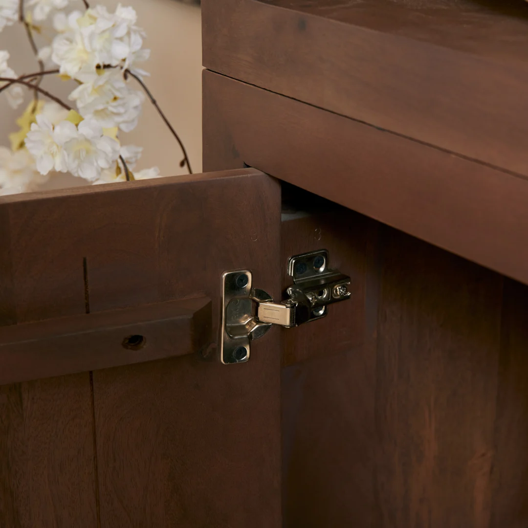 Een close-up van het houten oppervlak van Salontafel Walnoot Compact, met een zichtbaar metalen scharnierdetail en witte bloemen zacht vervaagd op de achtergrond.