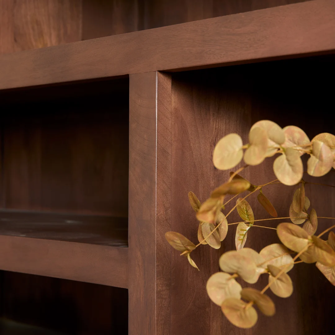 Close-up van de Salontafel Walnoot Compact, met de donkerbruine houten afwerking en de gestructureerde hoek, met gedroogde, ronde lichtgele bladeren op de voorgrond. Het compacte tafelblad lijkt leeg, wat het elegante vakmanschap benadrukt.
