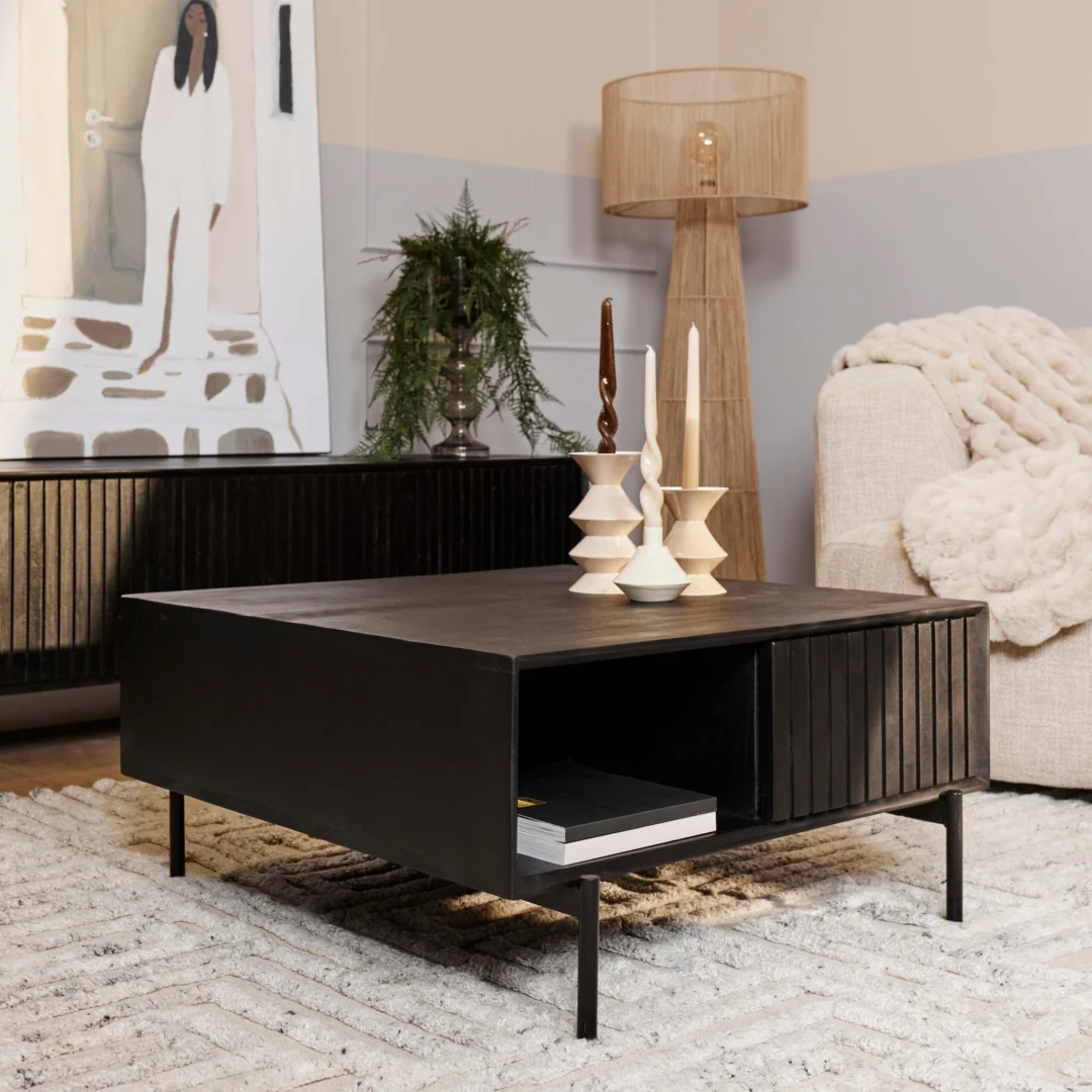 Een moderne woonkamer met de Salontafel 80 x 80 CM Vierkant Opbergvak met kaarsen, een beige vloerkleed met structuur, een lichte bank met een deken, een staande lamp, een plant en een kunstwerk van een vrouw in het wit aan de muur.